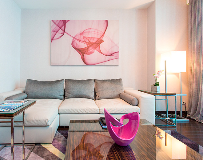 A gray and white couch with pink and white artwork hanging on the wall above.