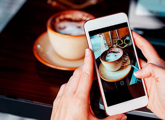 A person taking a close up photo of their cappucinno with their phone.