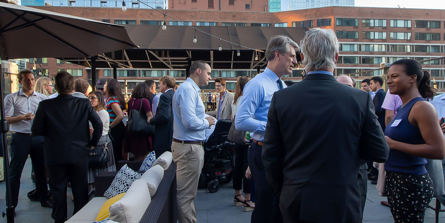 A group of business people talking on a rooftop terrace at dusk.