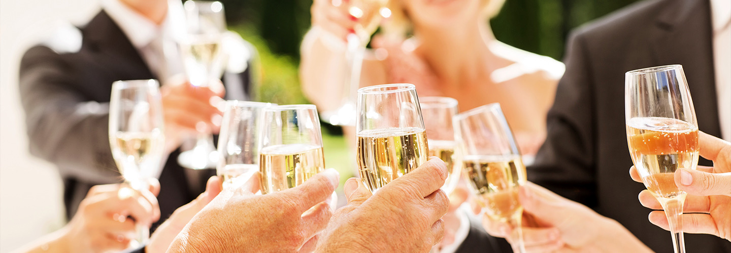 A group of wedding guests clinking glasses of champagne together outdoors with the sun shining.