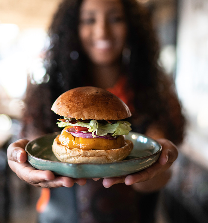 A woman holding a cheeseburger on a small round green plate.