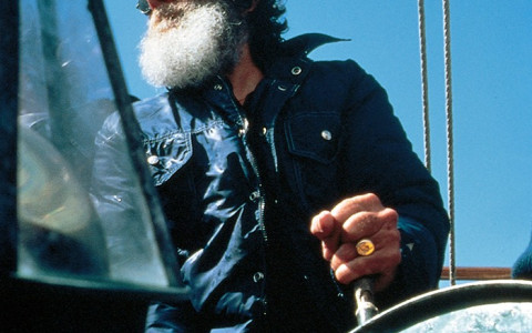 man with a beard and sunglasses steering a boat