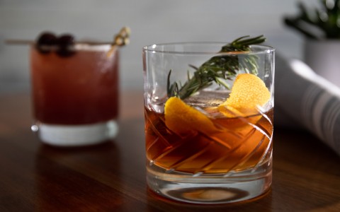 alcoholic beverage garnished with orange peel and rosemary