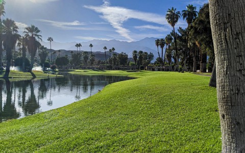 the sun shining over the golf course and large pond with mountains in the far distance