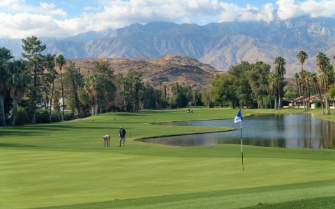a large mountain range in the distance and two people playing golf on the course