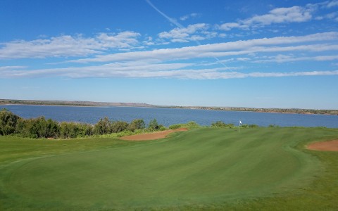 a portion of the golf course along a lake with bright blue skies above
