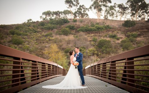 a bride and groom standing together on a bridge with a hill in the background
