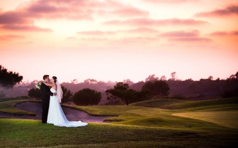 a bride and groom hugging on the golf course at dusk