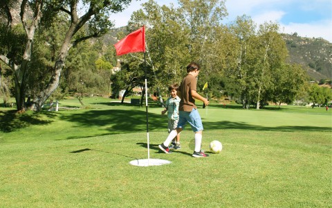 two young boys kicking a ball on the golf course