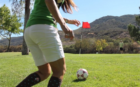 a close up of a girl kicking a soccer ball on the golf course