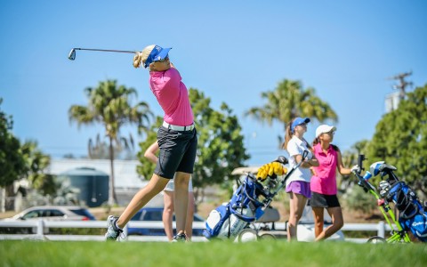 a woman swinging her club and looking forward with two other golfers standing to her left
