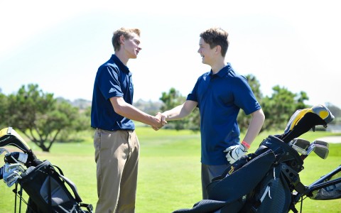 two young male golfers shaking hands on the golf course