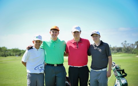 four young boys in golf attire posing for a photo on the golf course