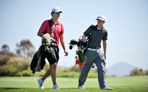 two young boys walking with their bags over their shoulder on the golf course