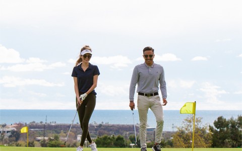 a smiling man and woman walking towards a yellow flagstick on the putting green