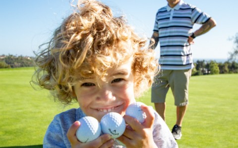 a young boy smiling with golf balls in his hands