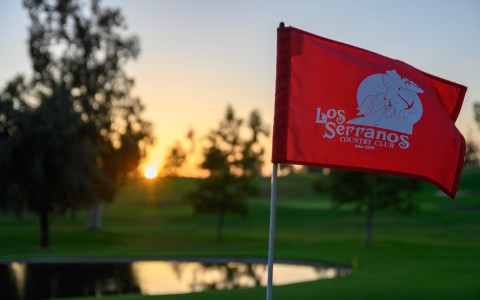 close up of a red flagstick and the sun setting in the background