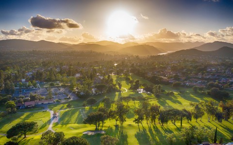 the sun shining bright over the mountains and golf course as it is setting
