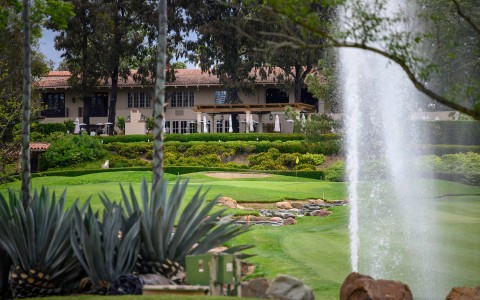 a golf course with a fountain and a light brown building located in the background