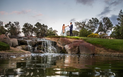 a small waterfall and a bride and groom to the right at sunset