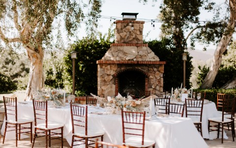 white linen covered tables and a large outdoor stone fireplace