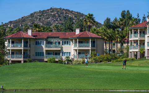tan multi-story buildings located near the golf course and a small hill in the distance