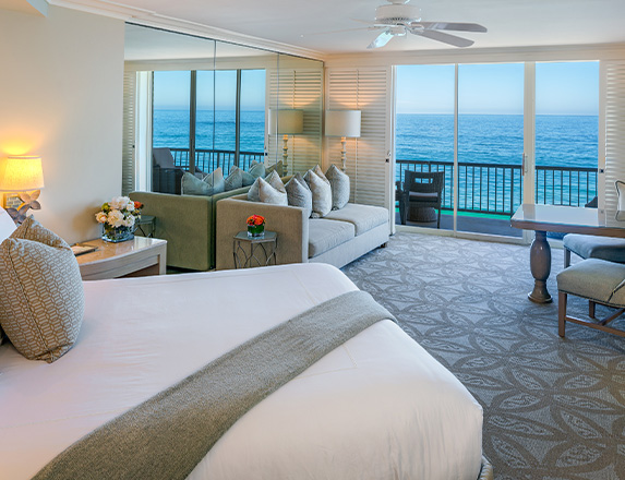 an elegant room with bed, sofa, and table that overlooks the ocean