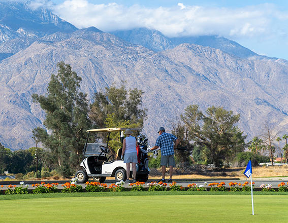 a man and woman next to their golf cart with a huge mountain in the distance