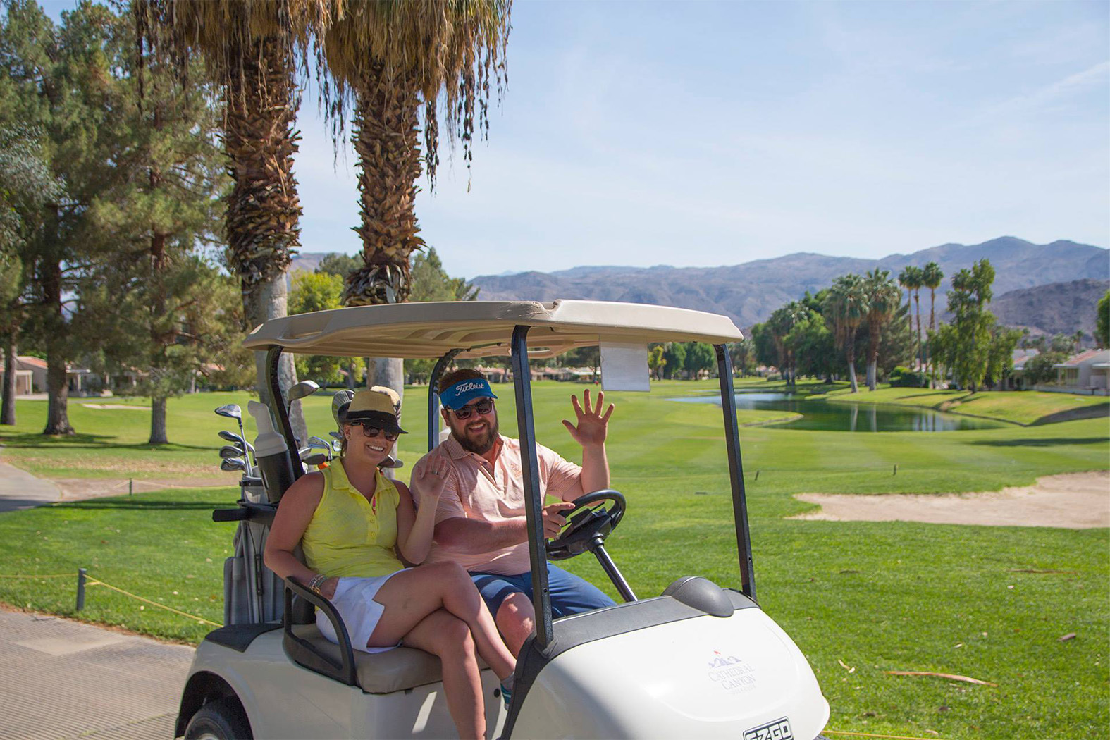 a smiling man and woman on a golf cart while waving 