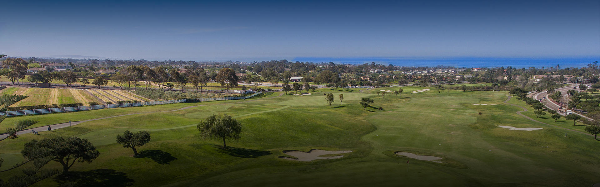 a panoramic view of the golf course with a view of the ocean in the far distance