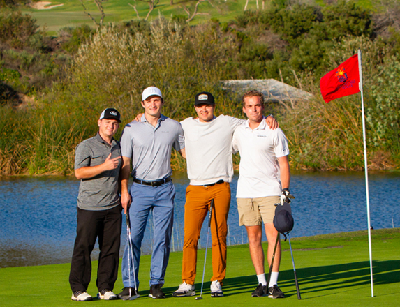  four men golfers standing on the course smiling and posing next to a red flagstick