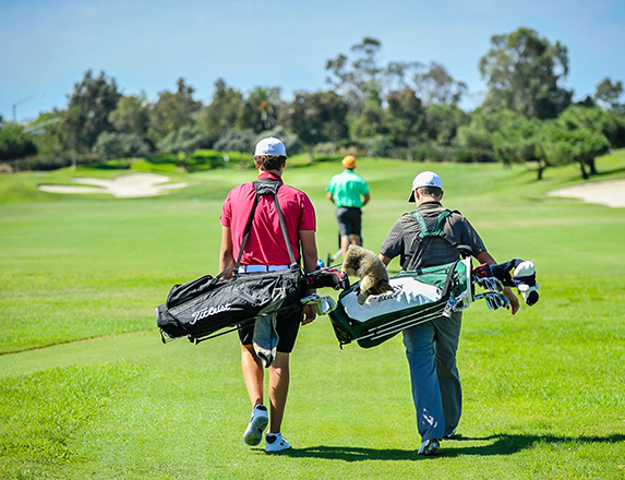 two young golfers walking behind another golfer on the course 