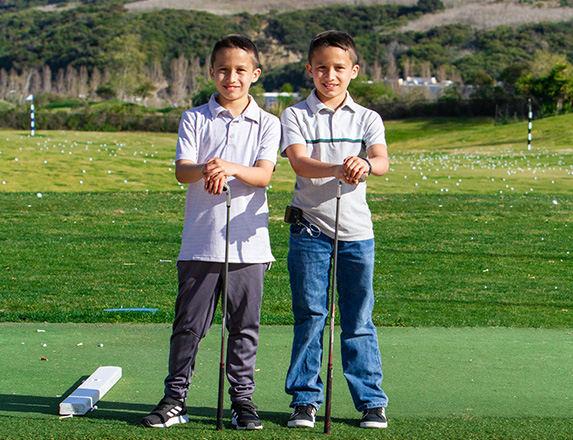 two boys posing with their golf clubs while standing next to the driving range