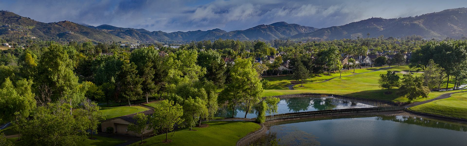 a bright green course with lots of trees and many mountains in the distance as well as a bridge over the water