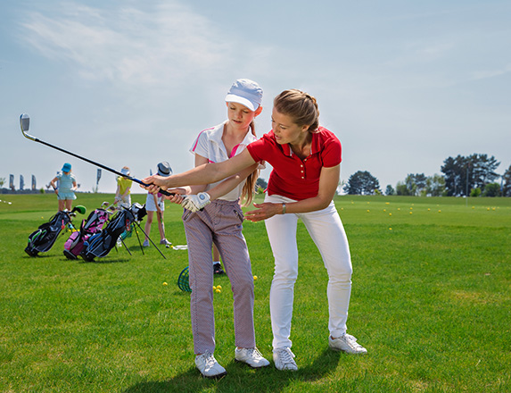 a woman showing a young girl how to swing the golf club