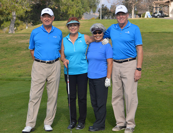 four golfers wearing blue shirts and posing while on the course