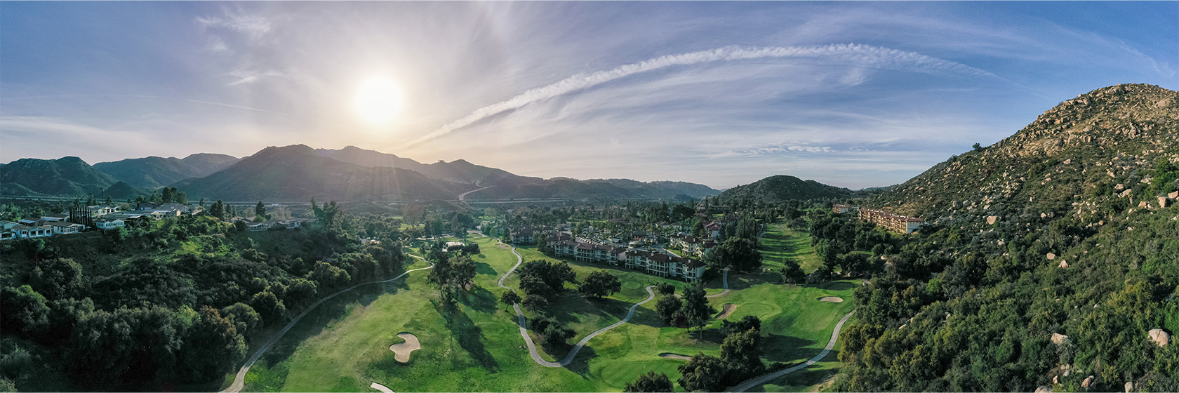 a drone shot of the sun setting over the mountains and golf course 