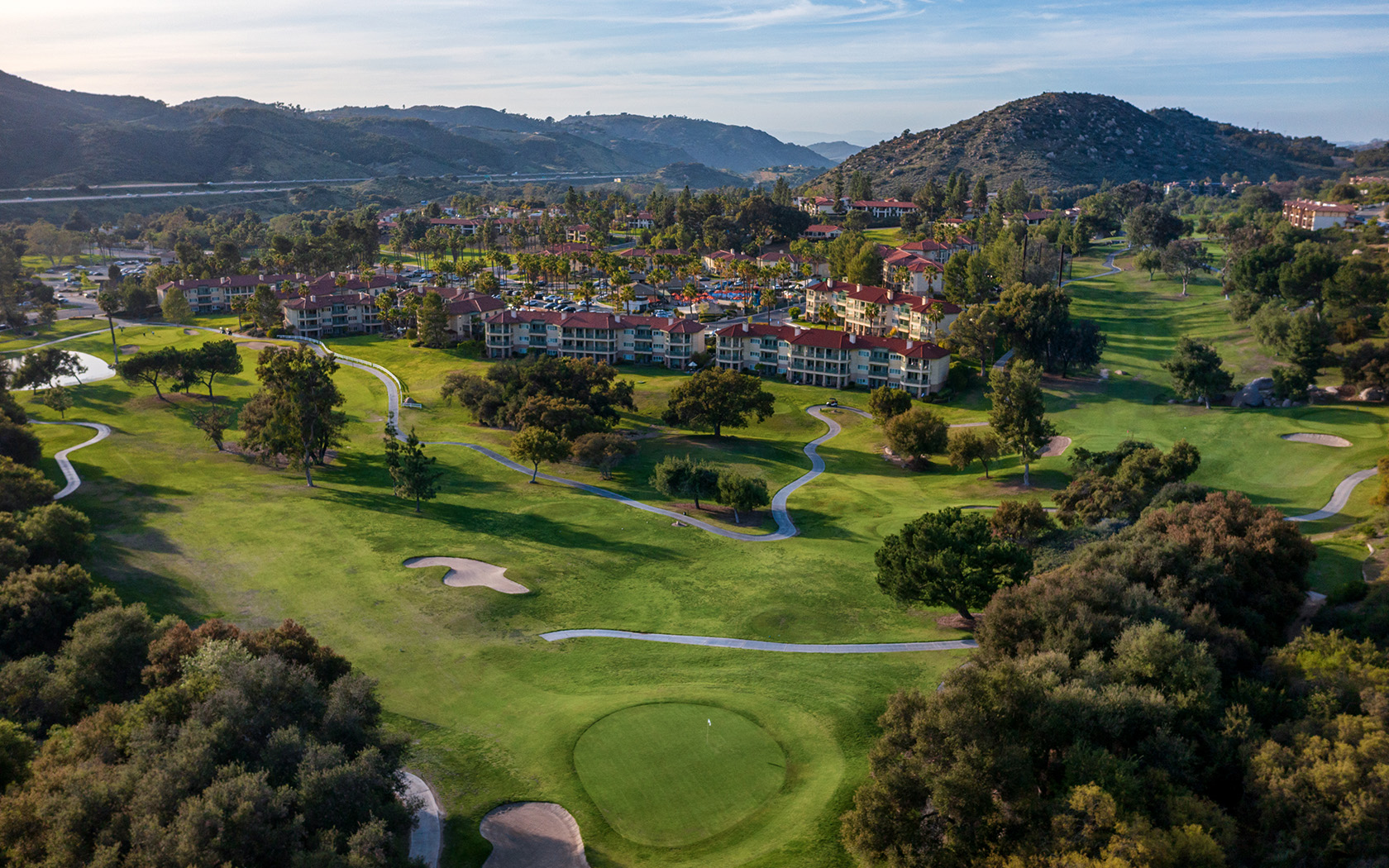 a drone shot of the golf course and property with many buildings and mountains in the distance