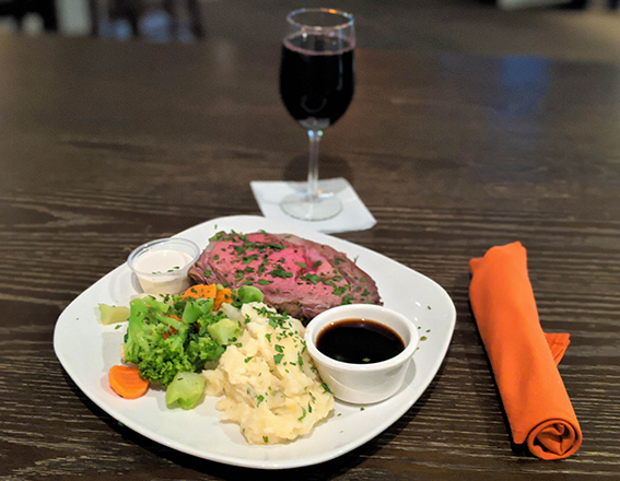 a prime rib dinner with mash potatoes, vegetables, and a glass of red wine