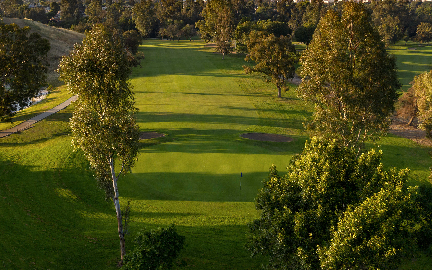 aerial view of the golf course with the shadows from the trees cast on it as the sun is setting to the left