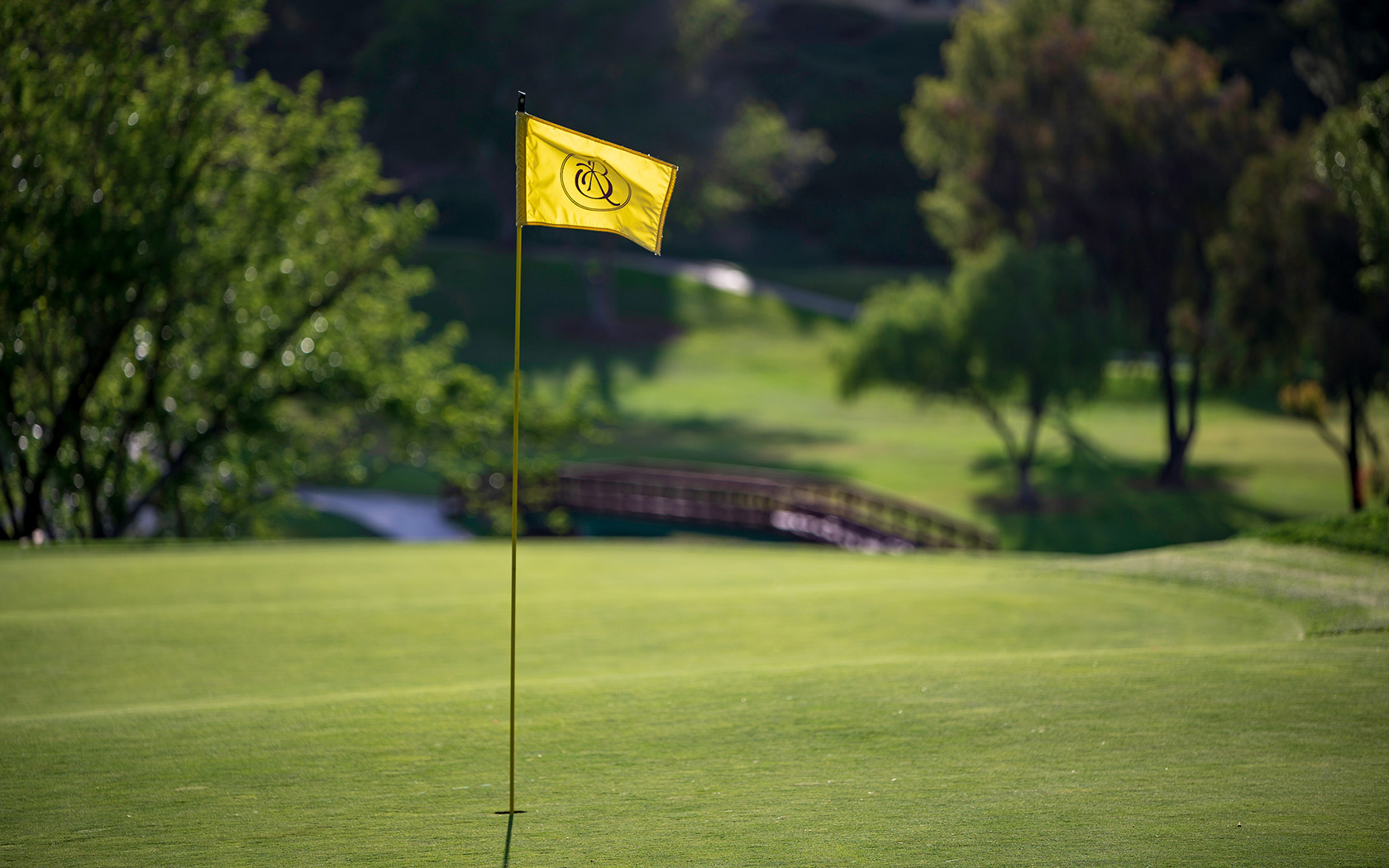 a close up of a yellow flagstick and a small wooden bridge in the background