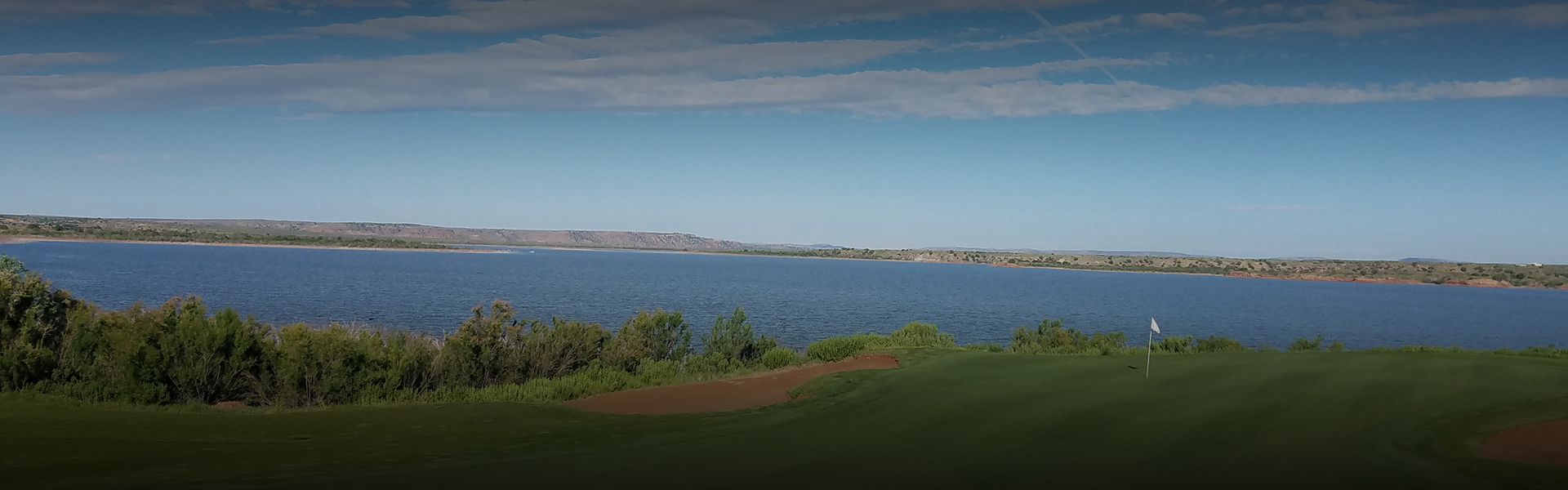 a dim image of clear blue skies over a large lake and golf course with small bushes lining the shore