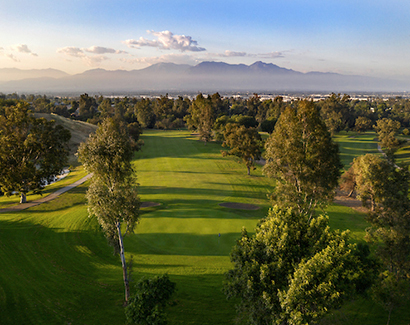 the sun setting to the left of the golf course with the mountains in the distance