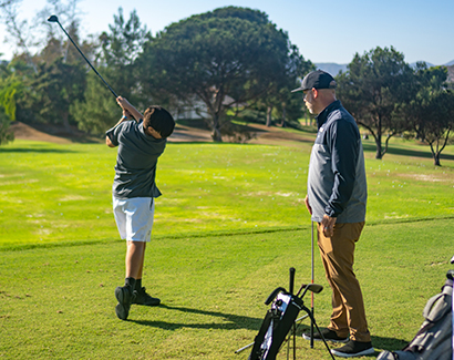 a young golfer practicing his swing while another person watches