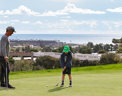 a young boy and his father playing golf on the course and a view of the ocean in the distance