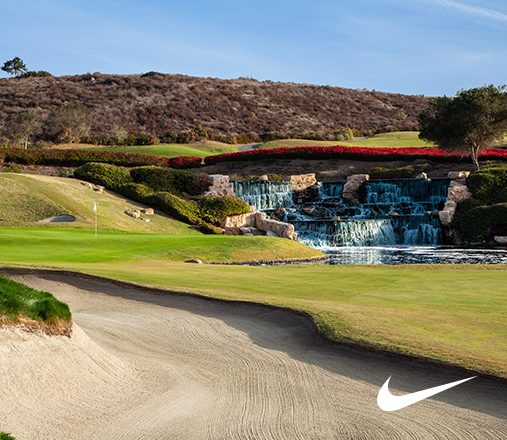 a small waterfall on the golf course with red flower bushes behind it and a nike logo to the bottom right