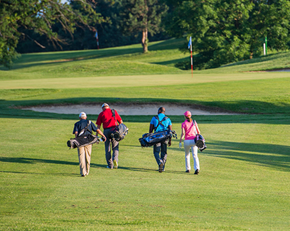 four golfers walking on the course with their golf gear during the day