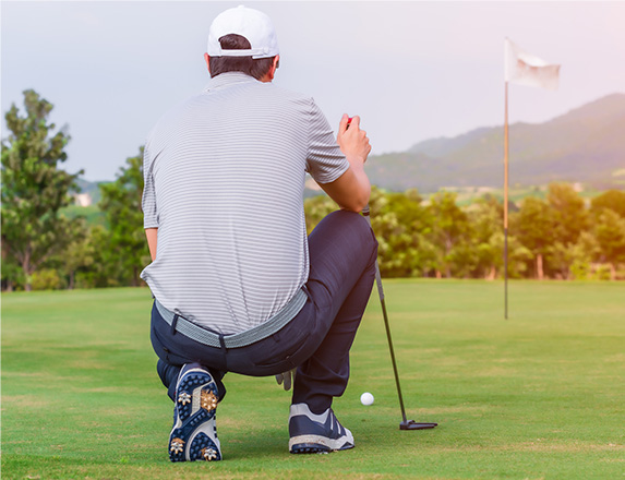 a man kneeling down on the green looking forward towards his golf ball