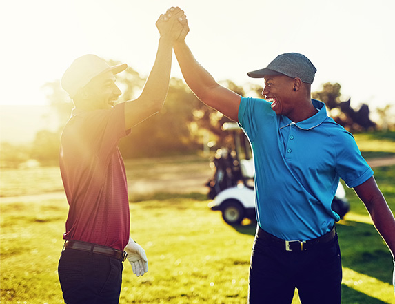 two smiling men celebrating on the golf course with their hands clenched together in the air