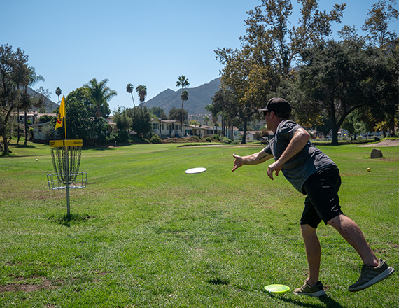 a male playing disc golf during the day with tall mountains in the distance